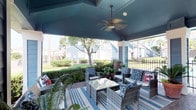 This single-story space combines a well-appointed covered outdoor living area with a thoughtfully designed interior. The covered patio is a standout feature, boasting a vaulted teal-painted ceiling with coffered detailing and a ceiling fan for year-round comfort. A full wicker seating arrangement, accented with blue and white patterned cushions and a striped area rug, creates an inviting outdoor lounge. The space opens to views of a landscaped yard with mature trees and neighboring structures, enclosed by a decorative iron fence and lush hedging.

Inside, the dining area showcases a distinctive round green marble pedestal table surrounded by woven rattan chairs, set atop a neutral area rug over dark concrete flooring. Recessed lighting illuminates the neutral-toned walls, which display a large-scale framed abstract artwork. A sliding barn door adds an industrial-chic architectural detail, while a set of aged, character-rich French doors provides a visual connection to adjacent spaces. The overall aesthetic blends eclectic and contemporary design elements, creating a curated, gallery-like ambiance throughout.