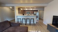 Located at 1608 East South Riverton Avenue in Spokane, WA, this well-appointed single-floor unit offers a thoughtfully designed layout with modern finishes throughout. The open-concept living and kitchen area serves as the heart of the home, where a spacious kitchen features dark espresso cabinetry, stainless steel appliances including a French door refrigerator, electric range, and microwave, all complemented by light quartz countertops and a large peninsula with bar seating for four. Pendant lighting adds a polished touch above the peninsula, while recessed lighting illuminates the kitchen workspace. Light wood-style flooring flows throughout the main living areas, creating a cohesive and bright atmosphere. The living room offers generous space with a window that brings in natural light and outdoor views of the surrounding greenery. The primary bedroom is carpeted and features a window, access to a walk-in closet, and an en-suite bathroom with a wide vanity, dark cabinetry, and a separate shower. A second bedroom is equally comfortable with carpet, a large window with outdoor views, and ample space. A second bathroom includes a vanity with dark cabinetry, a tub/shower combination, and light wood-style flooring, completing this well-rounded and functional home.