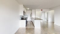 Located at 100 Cosburn Ave in Toronto's East York neighbourhood, this well-appointed one-bedroom, one-bathroom unit offers a clean, modern aesthetic throughout. The open-concept living and dining area is bathed in natural light from large windows that frame views of the surrounding cityscape, complemented by classic parquet hardwood flooring and a radiator heating system. Sliding glass doors lead to a private balcony, extending the living space outdoors.

The kitchen is thoughtfully designed with crisp white shaker-style cabinetry reaching to the ceiling, dark countertops, a light subway tile backsplash, and a full suite of stainless steel appliances including a stove, built-in microwave, and dishwasher. A generous kitchen island with a dark countertop provides additional workspace and casual dining potential.

The bedroom is a comfortable, well-proportioned room featuring a large window with an urban outlook, a radiator, and mirrored sliding closet doors that add depth to the space. The bathroom is finished in bright white subway tile from floor to ceiling, featuring a soaking bathtub with overhead shower, a pedestal sink, and polished tile flooring. Throughout the unit, white walls and consistent flooring create a cohesive and inviting atmosphere.