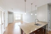This well-appointed one-bedroom, one-bathroom residence in Westborough, MA offers a thoughtfully designed single-level layout with a comfortable and functional floor plan. The open-concept living area flows seamlessly from the kitchen through the dining and living spaces, all finished with warm hardwood-style flooring that enhances the bright, airy atmosphere. The kitchen serves as a central hub, featuring a peninsula with granite countertops, an undermount sink with pendant lighting overhead, rich dark-wood cabinetry, and a full suite of stainless steel appliances including a refrigerator, range, and microwave. The combined dining and living areas provide generous room for both entertaining and everyday living, with natural light streaming in through large windows. The spacious primary bedroom is carpeted for comfort and includes a dedicated closet, with an additional closet available in the hallway. The full bathroom is finished with classic subway tile surrounding the tub-shower combination, light tile flooring, a dark-wood vanity with a white countertop, and a large mirror. Additional conveniences include a dedicated laundry area, utility room, and a private entrance, rounding out this practical and inviting Westborough residence.