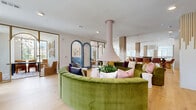 Located at 3712 Stewart Rd in Doraville, GA, this thoughtfully designed single-floor space offers a generous footprint across two distinct living areas and two dining areas. The interior is defined by an eclectic, contemporary aesthetic that balances bold color with refined architectural detail.

The main living area serves as the heart of the space, anchored by a striking circular green velvet sectional sofa surrounding a sculptural pendant fireplace column. Warm, wide-plank hardwood flooring runs throughout, complementing the crisp white walls and teal wainscoting accents. Decorative arched doorways in teal add visual depth and serve as elegant transitions between zones.

A secondary lounge area features floor-to-ceiling black-framed windows that flood the space with natural light and provide views of the surrounding greenery. Curated artwork, including Asian landscape prints and abstract pieces, adds cultural richness to the walls.

The dining areas include a casual high-top bar table with patterned upholstered seating and a more intimate meeting-style dining nook with a bold blue table, leather chairs, and tall windows. Translucent mesh partition walls offer a unique design element that subtly divides areas while maintaining visual openness. The overall ambiance is lively, welcoming, and artistically curated.