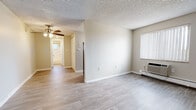 The Sterling Platinum is a one-bedroom, one-bathroom unit thoughtfully designed to maximize its compact footprint. The main living area greets residents upon entry through a solid white front door, showcasing light wood-style laminate flooring that extends throughout the common spaces. Neutral, warm-toned walls paired with white baseboards create a clean, cohesive aesthetic. A wall-mounted HVAC unit and baseboard heating ensure year-round climate comfort, while a window fitted with vertical blinds allows natural light to filter in.

The kitchen features white cabinetry with brushed nickel hardware, speckled stone-look countertops, and black appliances including an electric range and refrigerator, offering functional workspace within a compact layout.

The bedroom is carpeted in a neutral beige tone, providing a softer underfoot feel, and includes a baseboard heater. The textured popcorn ceiling is consistent throughout the unit.

The bathroom includes wood-style flooring, a white vanity, a full tub/shower combination with white tile surround, and a small window that provides natural ventilation. A hallway connects the living spaces efficiently, completing this straightforward and practical single-floor layout.