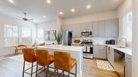 This thoughtfully designed single-floor residence offers a seamless blend of modern style and everyday functionality. The open-concept layout connects the kitchen, dining, and living areas into one cohesive, light-filled space. Light wood-look flooring runs throughout the main living areas, complementing the neutral white walls and recessed lighting overhead.

The kitchen is a standout feature, showcasing floor-to-ceiling gray shaker cabinetry, a crisp white quartz countertop island with bar seating, and a full suite of stainless steel appliances including a gas range, microwave, refrigerator, and dishwasher. A clean subway tile backsplash and ample natural light from nearby windows complete the space.

The living area is bright and welcoming, with large windows that invite natural light and provide views of the surrounding neighborhood. The space flows comfortably, offering room for relaxed seating arrangements.

Both bedrooms feature plush carpeting, generous windows with exterior views, and a calm, neutral palette that promotes rest and comfort.

The bathroom is elegantly appointed with floor-to-ceiling marble-style tile, a glass-enclosed shower, a gray vanity with quartz countertop, and a wide mirror — creating a refined, spa-like atmosphere. Every detail of this residence reflects a commitment to contemporary, quality living.