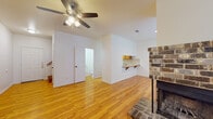 This two-floor residence is designed with a practical and cohesive layout, featuring warm hardwood flooring that runs throughout both levels. The main living area on the first floor is open and inviting, anchored by a classic brick fireplace and fitted with a ceiling fan overhead. Adjacent to the living area, a compact pass-through kitchen offers wood cabinetry, tile countertops and backsplash, a white electric range, a dishwasher, and a stainless steel sink — all efficiently arranged for ease of use. A half bathroom is conveniently located on this floor. Stairs from the main level lead up to the second floor, where the bedrooms are situated. Each room features rich hardwood flooring and ceiling fans, with windows providing natural light. One bedroom includes a closet with shelving and direct access to a full bathroom, which is outfitted with a tub-shower combination and tile surround. A second bathroom on this level includes a single vanity with wood cabinetry, a countertop sink, and a medicine cabinet mirror. Throughout the space, white walls create a clean, neutral backdrop that complements the warm wood tones, lending the home a bright and well-maintained atmosphere.