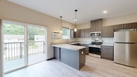 Located at 520 Tyler Rd in Red Wing, MN, this studio offers a thoughtfully designed single-floor layout that maximizes every square foot with functional, modern finishes. The open-concept kitchen is the centerpiece of the space, showcasing rich dark wood cabinetry, granite countertops, and a full suite of stainless steel appliances including a range, over-the-range microwave, and refrigerator. Pendant lighting hangs above the peninsula breakfast bar, providing both task lighting and a stylish focal point. Light hardwood-style flooring runs throughout the unit, creating a bright, cohesive feel. A sliding glass door in the kitchen/living area opens to a private balcony with outdoor views, allowing natural light to fill the space. The hallways are clean and well-lit, featuring white panel doors with dark hardware accents and ample closet access. The bathroom is finished with a walk-in shower stall equipped with a grab bar and chrome fixtures, set above charming mosaic tile flooring. Baseboard heating is present throughout, and a ceiling fan adds comfort to the living area. The neutral color palette and modern finishes give this studio a clean, move-in-ready appeal.