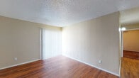 This single-floor unit offers a practical and straightforward layout designed for comfortable everyday living. The main living area greets you upon entry through a solid front door, showcasing warm wood-look flooring that extends throughout the common spaces. Textured walls and a popcorn ceiling add a classic character to the room, which also benefits from a sliding glass door fitted with vertical blinds, allowing natural light to filter in. A hallway connects the living area to the rest of the unit.

The kitchen is efficiently arranged with warm wood cabinetry providing ample upper and lower storage, granite-look countertops, and white appliances including an electric range and refrigerator. The wood-look flooring continues here, making for easy maintenance.

The bedrooms are carpeted in a deep, rich tone and each feature grid-pane windows that bring in natural light and views of surrounding greenery. The textured ceilings and neutral wall tones create a calm, understated atmosphere throughout.

The bathroom is clean and functional, featuring a full-size soaking tub with an overhead shower, white tile surround, and chrome fixtures. The overall ambiance of this unit is neutral and move-in ready, offering a solid foundation for personalization.