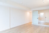 Located at 877 College St in Toronto's vibrant Little Italy neighbourhood, this modern one-bedroom, one-bathroom unit offers a thoughtfully designed single-floor layout. Light-toned hardwood flooring runs continuously throughout, lending warmth and visual continuity to the entire space.

The open-concept living and kitchen area forms the heart of the unit. The kitchen is outfitted with sleek white cabinetry, white quartz countertops, and a full suite of stainless steel appliances, including a refrigerator, electric range, built-in microwave, and dishwasher. Track lighting overhead ensures ample illumination across the cooking and dining areas. A frosted glass sliding door connects the main living space to the bedroom, maintaining an airy, open feel while providing privacy.

The bedroom is a bright, clean space featuring floor-to-ceiling black-framed windows that frame views of the surrounding College Street neighbourhood and allow generous natural light to fill the room. Clean white walls and the continuous hardwood flooring keep the aesthetic minimal and contemporary.

The bathroom is finished with white subway-style wall tiles and includes a full soaker tub with an overhead shower, an undermount sink with modern fixtures, and a large mirror. A well-proportioned hallway connects all rooms, featuring clean white walls with matte black door hardware throughout, consistent with the unit's modern design language.