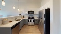 Located at 72 Elliot Ave in Quincy, MA, this single-floor residence showcases a contemporary design with a clean, open-concept layout and consistent modern finishes throughout. The kitchen is well-equipped with stainless steel appliances, including a refrigerator, range, microwave, and dishwasher. White upper cabinetry contrasts with gray lower cabinets, complemented by light countertops and wood-look flooring. A peninsula with pendant lighting and bar seating connects the kitchen to the main living area, creating an ideal space for entertaining. The living room is bright and spacious, featuring large sliding glass doors that open to a private balcony with outdoor views, allowing abundant natural light to fill the space. The bedrooms feature plush carpeting and generous windows that bring in natural light and exterior views. The bathroom is finished with wood-look flooring, a gray vanity with white countertop, and ample storage. A hallway with closet space provides practical utility. Throughout the unit, neutral tones and modern fixtures create a cohesive, inviting ambiance suited for comfortable everyday living.
