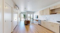 This thoughtfully designed one-bedroom, one-bathroom residence at 310 Bugatti Ave in South Salt Lake offers a clean, modern aesthetic throughout. Light-toned hardwood-style flooring flows seamlessly across the entire unit, creating a cohesive and airy feel.

The open-concept kitchen is well-appointed with light wood cabinetry, white subway tile backsplash, and a full suite of stainless steel GE appliances, including a French door refrigerator and electric range. The adjoining living room is bathed in natural light from large floor-to-ceiling windows and a sliding glass door that opens to a private balcony, offering sweeping views of the surrounding mountains and cityscape.

The bedroom is a bright, comfortable retreat featuring its own large window framing impressive mountain views, a wall-mounted mini-split HVAC unit, and direct access to a spacious walk-in closet outfitted with dual shelving systems on both sides.

The bathroom maintains the home's modern design language with light wood vanity cabinetry, a white countertop, and hardwood-style flooring. Accessibility-conscious grab bars are thoughtfully integrated throughout. Clean white walls and recessed lighting complete the polished, contemporary ambiance found throughout this well-planned residence.