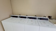 This single-floor utility space is purpose-built to deliver essential shared amenities in a clean, organized environment. The laundry area is equipped with a row of commercial-grade Speed Queen washers and dryers, arranged side by side for efficient, high-capacity use. Each machine features a digital control panel, reflecting a modern, user-friendly design suited for frequent, heavy-duty laundry needs. The neutral, warm-toned walls and bright lighting keep the space feeling tidy and functional.

Adjacent to the laundry area is a dedicated storage section, where a series of individually numbered lockers are neatly arranged along the wall. Each locker is clearly marked with a bold stenciled number and secured with its own latch, providing residents or users with private, organized storage solutions. The lockers are finished in a clean white, consistent with the overall utilitarian aesthetic of the space.

Together, these two areas form a well-organized, practical utility floor that prioritizes convenience and functionality. The layout is straightforward and efficient, making it easy to navigate between the laundry and storage sections. The space is maintained to a high standard of cleanliness, ensuring a comfortable and reliable experience for all who use it.