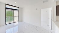 Located at 1 Curtiss Pkwy in Miami Springs, FL, this modern 3-bedroom, 3-bathroom unit offers a clean, contemporary design throughout. Polished marble-look porcelain tile flows seamlessly across the entire space, lending an air of sophistication and continuity to every room. The open-concept kitchen is a standout feature, showcasing dark wood cabinetry, a light quartz peninsula with an undermount sink, and a full suite of stainless steel appliances including a range, built-in microwave, dishwasher, and French door refrigerator. Rail lighting overhead adds a modern touch while illuminating the kitchen and adjoining living area. The living space is bright and airy, benefiting from large black-framed windows that invite natural light and offer views of lush greenery outside. Each of the three bedrooms is finished with the same polished tile flooring and crisp white walls, providing a clean, neutral canvas. The three bathrooms are uniformly appointed with marble-look tile on both floors and walls, paired with modern vanities featuring gold-toned hardware and ample mirror space. Two closets and a hallway round out the thoughtfully arranged floor plan, offering practical storage solutions throughout this stylish Miami Springs residence.