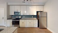 Located at 257 Broadway Street in the heart of Asheville, NC, this single-floor unit offers a thoughtfully designed open-concept layout that seamlessly connects the living, dining, and kitchen areas. The living space features warm hardwood-style flooring, neutral-toned walls, and a ceiling fan with integrated lighting, creating a bright and comfortable atmosphere. A sliding glass door opens to an outdoor balcony, allowing natural light to fill the room and providing a pleasant connection to the outdoors.

The kitchen is a standout feature, boasting tall white cabinetry that reaches the ceiling for ample storage, granite countertops, a teal accent backsplash, and a full suite of stainless steel appliances including a range, microwave, and refrigerator. A peninsula with matching granite adds additional prep and seating space, bridging the kitchen with the living area.

The bedroom is generously proportioned, finished with plush carpeting, dual windows with slatted blinds, and a ceiling fan, ensuring comfort and natural light. The bathroom is clean and functional, featuring tile flooring, a granite-topped vanity with undermount sink, and a well-organized layout that includes additional access to a utility or laundry area. Throughout the unit, consistent finishes and modern fixtures contribute to a cohesive, move-in-ready aesthetic.