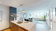 Unit 1613 at 930 McCarter Highway is a well-appointed one-bedroom, one-bathroom residence offering a thoughtfully designed open-concept layout with warm hardwood flooring throughout. The combined kitchen and living area serves as the heart of the home, anchored by floor-to-ceiling windows that frame sweeping city skyline views and flood the space with natural light. The kitchen is outfitted with stainless steel appliances, two-tone cabinetry in slate blue and wood-toned finishes, white quartz countertops, and a peninsula with bar seating, accented by elegant pendant lighting with brass hardware. The living area comfortably accommodates generous seating and benefits from the same panoramic urban views. The bedroom is a serene retreat, featuring its own large window with skyline views, hardwood flooring, and ample space for a full suite of furnishings. A dedicated closet provides convenient storage. The bathroom is finished with light marble-style tile flooring, a wood-accented vanity, and matte black fixtures, lending a clean, modern aesthetic. The unit's crisp white walls, contemporary design details, and high-floor positioning combine to create a bright, sophisticated living environment.