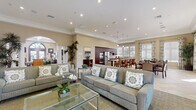 Located at 1510 Santa Diana Rd in Chula Vista, CA, this single-story community clubhouse offers a well-appointed and thoughtfully designed gathering space. The open-concept lounge and living area serves as the heart of the facility, featuring a striking stacked-stone fireplace flanked by built-in dark wood shelving, a wall-mounted TV, and plush seating arranged over patterned carpeting and polished tile flooring. Crown molding and recessed lighting throughout lend a refined, cohesive aesthetic.

The full kitchen is outfitted with rich dark wood cabinetry, quartz countertops, a mosaic tile backsplash, stainless steel appliances including a gas cooktop and double wall oven, and a central island with bar seating. It opens directly to a casual dining area bathed in natural light from large windows dressed with decorative valances.

A separate formal dining room accommodates a large table with elegantly upholstered high-back chairs beneath a tray ceiling, while an additional media and meeting room features dark wood entertainment units and a chandelier. A sun-drenched alcove with floor-to-ceiling windows provides a quiet workstation nook. Glass double doors lead to a covered outdoor patio with seating, completing this versatile and welcoming community space.