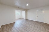 This single-floor residence offers a bright and functional layout designed for comfortable everyday living. The main living and dining areas flow openly into one another, unified by warm wood-style laminate flooring that runs throughout the primary spaces. Large windows in the connected living zones invite natural light and offer views of surrounding greenery, creating an airy and welcoming atmosphere. Crisp white walls and textured ceilings complement the clean aesthetic found throughout the home.

The kitchen is a standout feature, showcasing white cabinetry, granite-look countertops, a classic subway tile backsplash, and a freestanding electric range with an overhead ventilation hood — a practical and visually appealing setup for home cooking.

The bedroom is finished with plush wall-to-wall carpet for comfort and includes a closet for storage. A full bathroom serves the home, complete with a pedestal sink, a mirrored medicine cabinet, and a shower-tub combo, all finished in clean white tones with tile flooring.

Additional interior spaces include a hallway with access to closets and utility connections, as seen in the dollhouse overview. The home's neutral palette and updated finishes throughout provide a versatile canvas well-suited to a variety of living arrangements.