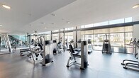 Located at 1010 S Pearl Expy in Dallas, TX, this two-story fitness center offers a comprehensive and thoughtfully designed workout facility. The main floor is anchored by a generously sized open gym area bathed in natural light from floor-to-ceiling windows, which provide views of the surrounding outdoor spaces. This level houses an extensive array of cardio machines—including treadmills, ellipticals, and stair climbers—alongside a wide selection of strength and resistance equipment. Large mirrors line the walls, enhancing the sense of openness throughout the space. A dedicated spin studio on this floor features a full lineup of Spinning bikes, a large wall-mounted display screen, and accessory storage, creating an immersive cycling experience. Adjacent areas provide space for functional and free-weight training, complete with dumbbell racks and benches. A staircase with sleek metal railings connects the main floor to the upper level, which features warm hardwood flooring and a versatile studio space equipped with TRX suspension trainers, resistance tools, stability balls, and mirrored walls—ideal for group classes or individual training sessions. Teal accent walls add a modern, energetic aesthetic throughout, while recessed and pendant lighting complement the abundant daylight. A utility room and closet support day-to-day operations seamlessly.
