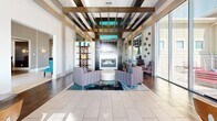 This well-appointed clubhouse in Broomfield, Colorado, offers a thoughtfully designed single-floor layout that balances social gathering with relaxed comfort. The dual entrance areas welcome visitors with light tile flooring, soaring ceilings, vibrant teal accent chairs, and decorative wall art, setting an upscale tone throughout. A central hallway connects the various spaces seamlessly.

The expansive living room serves as the heart of the clubhouse, anchored by a sleek fireplace with a dark wood surround and flanked by bold exposed ceiling beams with teal-lit accent shelving above. Large windows flood the area with natural light, while stylish lounge seating and large-scale artwork contribute to the modern aesthetic. A billiards table provides an engaging recreational focal point.

The combined kitchen and dining area features a generous island with bar seating, dark cabinetry, stainless steel appliances, and pendant lighting — ideal for hosting events or casual gatherings. The adjacent dining space opens to views of the outdoor pool area through floor-to-ceiling windows dressed with elegant sheer curtains.

The patio extends the entertaining space outdoors, offering poolside views and alfresco seating. Throughout, a cohesive palette of warm grays, teal accents, and rich wood tones creates a sophisticated and inviting atmosphere.