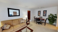 This single-floor residence offers a well-organized layout that connects key living spaces in a functional and comfortable flow. The combined living and dining area forms the heart of the unit, finished with light-colored carpet and white walls that create a bright, neutral backdrop. The living area includes a wall-mounted air conditioning unit, a baseboard heating system, and a large sliding glass door dressed with vertical blinds, allowing natural light to fill the space. A wall mirror adds depth to the room. Adjacent to the living area, the dining space is defined by a ceiling fan with a light fixture overhead and is large enough to comfortably accommodate a round table with seating for four.

The galley-style kitchen features warm wood cabinetry on both sides, laminate countertops, a stainless steel sink, and white appliances including a refrigerator, dishwasher, and electric range. Track lighting overhead provides ample task illumination, and light tile flooring completes the practical design.

Both bedrooms are carpeted and include windows that bring in natural light, with baseboard heating along the walls. Each room offers generous closet storage, including a set of sliding wood-panel closet doors in one bedroom. The full bathroom presents a tub-shower combination with a curtain rod, a vanity with storage below, and classic mosaic tile flooring.