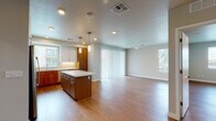 This single-floor residence features a contemporary design with warm wood-look flooring carried consistently throughout every room. The open-concept kitchen and living area form the heart of the unit, where a well-appointed kitchen stands out with a two-tone cabinet scheme pairing warm walnut-toned lower cabinets with crisp white upper cabinetry. A generous central island with a white quartz countertop provides both prep space and casual seating. Stainless steel appliances, including a refrigerator, range, microwave, and dishwasher, complete the kitchen. Pendant lighting above the island and recessed ceiling lights illuminate the space, while a window above the sink brings in natural light. The kitchen flows seamlessly into a spacious living area featuring windows on multiple walls and a sliding glass door, filling the room with natural light. A ceiling fan adds practical comfort. The full bathroom includes a single-sink vanity with walnut cabinetry, a large mirror, and a tub-shower combination. A second bathroom functions as a combined bathroom and laundry room, housing a washer and dryer alongside a single-sink vanity. The bedroom is a quiet, neutral room with a window and direct access to a walk-in closet fitted with multiple shelving tiers and hanging rods.