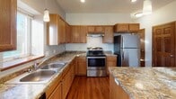 Located at 2321 Links St in Mankato, Minnesota, this single-floor home offers a practical and comfortable layout with a clean, neutral design throughout. The kitchen is a standout feature, equipped with warm oak cabinetry, stone-look countertops, stainless steel appliances including a refrigerator and range, a double sink, and a central island with pendant lighting — all set atop rich hardwood flooring. The open living area extends from the kitchen and benefits from generous natural light streaming through windows, highlighting the continuity of the hardwood floors and creating a bright, welcoming atmosphere. Multiple bedrooms are carpeted for comfort, each featuring windows that bring in natural light and outdoor views. The primary bedroom includes a tray ceiling detail, adding architectural interest. Two bathrooms serve the home — one a full bath with a tub/shower combination, and a half bath — both finished with stone-tile flooring, oak vanity cabinetry, and framed mirrors with stylish light fixtures. A dedicated laundry area with a full-size washer and dryer provides added convenience. Solid wood interior doors with classic paneling are featured throughout, reinforcing the home's cohesive and traditional character.