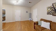 Located at 617 Richardson St in Simpsonville, SC, this single-floor space offers a comfortable and efficiently designed layout that combines living and dining functions within one open area. Warm, light-toned hardwood-style flooring runs throughout, lending a cohesive and inviting feel to the entire space.

The living area is thoughtfully arranged, featuring a wall-mounted flat-screen television and a ceiling fan with integrated lighting that provides both comfort and illumination. A track lighting fixture adds additional brightness, ensuring the space feels well-lit at all times. Neutral beige walls create a calm, versatile backdrop throughout.

A defined dining nook accommodates a wooden table and chair set, ideal for everyday meals. Adjacent to the dining area, a charming barn-style door leads to a small kitchenette or utility alcove, complete with a countertop appliance setup and a white console table — adding a touch of farmhouse character to the space.

Two interior doors along the back wall provide access to additional rooms or storage, maintaining a clean and organized flow. A textured ceiling adds subtle architectural detail overhead. The overall ambiance is warm, practical, and move-in ready, making this Simpsonville space a functional and comfortable option for everyday living.