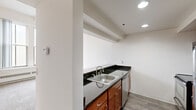 This 1-bedroom, 1-bathroom residence is thoughtfully designed to maximize its compact footprint across a single floor. The kitchen is a standout feature, equipped with stainless steel appliances including a refrigerator, range, and over-the-range microwave. Rich wood cabinetry pairs with dark granite countertops, which extend along the breakfast bar that opens toward the living area — creating a connected, open feel between the two spaces. Recessed lighting illuminates the kitchen efficiently, while wood-style flooring adds a clean, modern touch.

The living area features neutral carpet and clean white walls, offering a versatile canvas for furnishing. The bedroom is a comfortable, well-proportioned room with plush carpet, a large double-pane window that brings in natural light, and a built-in closet with shelving and a hanging rod. High ceilings in the bedroom add a sense of openness beyond the room's physical dimensions.

The bathroom maintains the same dark granite countertop found throughout the unit, complemented by a wood-vanity cabinet, a large mirror, tile flooring, and a full soaking tub with a tiled surround. The consistent use of dark granite and warm wood tones across the kitchen and bathroom creates a cohesive aesthetic throughout this well-designed residence.