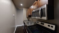 Located at 631 W Lexington Street in Baltimore, MD, this single-floor unit offers a well-appointed interior with a consistent design language throughout. Dark hardwood flooring runs across the space, providing a warm contrast to the cool gray-toned walls and crisp white baseboards.

The kitchen is designed as an efficient galley layout, featuring rich medium-toned wood cabinetry with sleek hardware, dark granite countertops with a double-basin stainless steel sink, and a full suite of stainless steel appliances including an electric range, over-the-range microwave, dishwasher, and refrigerator. Recessed lighting illuminates the workspace effectively.

The bathroom is a standout feature, finished with large-format travertine-style tile on the floors and walls. A frameless glass-enclosed walk-in shower with a rainfall-style showerhead anchors the room, complemented by a dark vanity with a white countertop, adding a refined, spa-like quality.

The remaining rooms are open, neutrally painted spaces ready for a variety of uses. One room benefits from a window with exterior views, allowing natural light to enter. Classic six-panel white interior doors and white trim throughout maintain a clean, traditional aesthetic that ties the unit together cohesively.