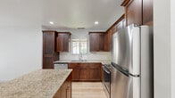 Located at 1465 W Deer Crest St in Meridian, Idaho, this two-story home offers a thoughtfully designed layout across two levels. The kitchen serves as a central highlight, featuring rich dark wood cabinetry, granite countertops, a classic white subway tile backsplash, and a full suite of stainless steel appliances including a refrigerator, range, microwave, and dishwasher. A kitchen island with matching granite provides additional prep and dining space. Light hardwood flooring flows through the kitchen and into the adjacent living area, which is bathed in natural light through a sliding glass door that opens to a view of the outdoors. The bathrooms are finished with granite-topped vanities, hardwood-style flooring, and clean white fixtures, including a full tub-shower combo in one bath. The bedrooms are carpeted and bright, each featuring windows with blinds that invite natural light. The lower level includes additional open living space with hardwood-style flooring and staircase access. Throughout the home, white walls and recessed lighting create a clean, well-lit atmosphere that complements the warm wood tones and stone finishes found in each room.