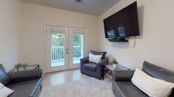 This single-floor residence at 2309 Evermore Way in Wilmington, NC offers a well-organized layout with multiple bedrooms, a galley-style kitchen, two bathrooms, and a comfortable living area. The kitchen is outfitted with white shaker cabinetry, granite countertops, a subway tile backsplash, stainless steel appliances, and light wood-look flooring, creating a clean and functional cooking space. The living area features carpet flooring, a wall-mounted flat-screen TV, and French doors that open directly to a private balcony overlooking greenery, allowing natural light to flow in. The bedrooms are carpeted and neutral in tone, with each offering generous wall space and room for a desk and dresser. Select bedrooms include large windows with tree-lined views, while at least one features a walk-in closet. The bathrooms are well-appointed, with one showcasing warm stone-tile flooring and a shower-tub combination, and the other offering a clean white vanity with a large mirror. Throughout, the space maintains a consistent neutral color palette with light walls and bright finishes, contributing to an open and airy ambiance suited for comfortable everyday living.