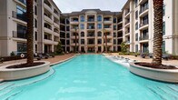 Located at 1916 W Gray St in Houston's prestigious River Oaks area, this ground-floor amenity space is situated within a striking multi-story residential complex defined by its European-inspired architecture, arched windows, and neutral stone façade. The building surrounds a beautifully landscaped central courtyard featuring a large resort-style pool with crystal-clear turquoise water, flanked by tall palm trees and lounge seating — a serene retreat within an urban setting.

The interior space features a practical, single-floor layout with rustic cobblestone-style brick flooring that carries throughout, lending warmth and texture to the environment. The entry corridor is clean and well-proportioned, with crisp white walls, crown molding details, and steel-framed glass doors that connect seamlessly to the outdoor courtyard. Accessible restroom facilities are conveniently positioned near the entrance.

The main room offers an open layout with high ceilings, neutral walls, and an octagonal floor detail that serves as a visual anchor. Double doors and a glass-paneled side entry provide multiple access points, while a gated black iron entry from the exterior leads directly to the pool courtyard. The space is well-suited for event or amenity use, combining functional infrastructure with the refined aesthetic of its surrounding complex.