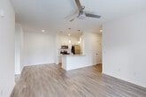 This single-story, one-bedroom, one-bathroom unit offers a thoughtfully arranged floor plan that maximizes its efficient footprint. Light-toned wood-look flooring runs continuously throughout, contributing to a cohesive and clean aesthetic. The open-concept living and kitchen area forms the heart of the unit, anchored by a central peninsula with a granite countertop and an undermount sink. The kitchen is outfitted with white shaker-style cabinetry, stainless steel appliances including a range, microwave, and refrigerator, and pendant lighting hanging above the peninsula. The living area benefits from a ceiling fan and French doors that allow natural light to filter in and provide outdoor access. The bedroom is a comfortable size, featuring a ceiling fan, a large window overlooking the exterior, and direct access to a dedicated closet with built-in shelving. The full bathroom includes a white shaker vanity topped with granite, a large mirror, and a tub-shower combination. A dedicated laundry room houses a full-size washer and dryer with overhead wire shelving, adding notable everyday convenience to this well-appointed unit.