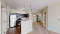This single-floor residence offers a well-designed open-concept layout that seamlessly connects the kitchen and living areas. The kitchen is a standout feature, equipped with a full suite of stainless steel appliances, including a refrigerator, electric range, built-in microwave, and dishwasher. Rich dark cabinetry with sleek hardware pairs with granite countertops and a classic white subway tile backsplash to create a polished, contemporary aesthetic. A peninsula with pendant lighting overhead provides additional prep space and serves as a natural divider between the kitchen and the carpeted living area. Crown molding and an arched architectural detail add refined character to the space, while built-in shelving offers practical storage. The bedrooms are carpeted and filled with natural light through generously sized windows. Bathrooms echo the kitchen's design language, featuring matching dark cabinetry, granite countertops, and tiled shower-tub combinations with wood-look flooring. The primary bathroom includes a wide vanity with an undermount sink. A spacious walk-in closet with wire shelving provides abundant storage, completing this functional and cohesive living space.