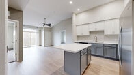 This thoughtfully designed two-bedroom, one-bathroom unit offers a well-organized single-floor layout with modern finishes throughout. The open-concept kitchen serves as the centerpiece of the living area, featuring a two-tone cabinet design with white upper cabinetry and gray lower cabinets, a central island with a white countertop, and a full suite of stainless steel appliances including a refrigerator, range, microwave, and dishwasher. Light wood-style flooring runs seamlessly through the kitchen and living areas, enhancing the bright, cohesive feel of the space.

The living room benefits from vaulted ceiling details, a ceiling fan, and sliding glass doors that open to a private balcony, allowing natural light to fill the room. Both bedrooms feature plush carpet flooring and natural light from windows. The primary bedroom offers a comfortable footprint, while both rooms include sliding-door closets with built-in shelving for organized storage.

The full bathroom is finished with a gray vanity, white countertop, and light wood-style flooring. A dedicated laundry room houses a full-size washer and dryer, adding practical convenience to the overall layout.