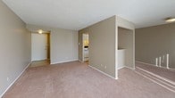 This single-floor residence presents a straightforward and functional layout designed for comfortable everyday living. The living area is generously sized, featuring soft wall-to-wall carpeting in a neutral tone and a textured ceiling that adds subtle visual interest. Warm beige and taupe wall colors carry consistently throughout the space, creating a cohesive and calm ambiance. A large vertical-blind window allows natural light to filter in, brightening the open feel of the room. The kitchen is efficiently arranged with ample white cabinetry above and below the countertops, providing notable storage. A double-basin stainless steel sink, light-toned countertops, and a full-size white refrigerator and range complete the kitchen's practical setup. Under-cabinet lighting adds warmth to the workspace. The bedroom is well-proportioned with the same plush carpeting found throughout, neutral walls, and a built-in closet with bifold doors that offer organized storage space. Natural light streams through a window, casting bright patterns across the floor. The bathroom features tile flooring, a single-sink vanity with wood-toned cabinetry, a wall-mounted mirror with overhead lighting, and a toilet, all within a clean and compact layout. Together, these spaces form a well-maintained, move-in ready residence suited for practical, comfortable living.