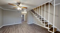 This two-story home offers a practical and well-organized layout across two floors, with the main living areas on the ground level and bedrooms situated above. The first floor features a spacious living area with wood-look laminate flooring, neutral gray walls, crown molding, a textured ceiling, and a ceiling fan with light fixture. An open staircase with white railings and dark wood treads connects the two floors, adding a structural focal point to the main living space. The kitchen is equipped with white cabinetry, gray laminate countertops, a double-basin sink, and a black refrigerator, with a window providing natural light. A full bathroom on the upper level includes a tub-shower combo with tile surround, a toilet, and built-in shelving for storage. The primary bedroom is generously sized and features built-in shelving, a ceiling fan, and access to a closet. The second bedroom benefits from multiple windows that bring in natural light and showcases textured walls with wood-look flooring. Both bedrooms offer comfortable proportions and ample closet storage. Throughout the home, consistent wood-look flooring, neutral tones, and ceiling fans create a cohesive and functional living environment.
