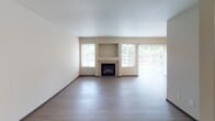 This two-story residence located in Tacoma, Washington offers a well-organized layout spread across two levels, connected by a staircase with a wood-railed banister. The entry-level hallway, finished with light wood-tone luxury vinyl plank flooring, leads toward the main living area, which features a fireplace visible from the corridor.

The kitchen is designed with white shaker-style cabinetry, light granite-look countertops, a peninsula with a breakfast bar overhang, stainless steel appliances including a range, refrigerator, and built-in range hood, along with a stainless steel double sink. The open sightlines between the kitchen and living area support an efficient, functional flow.

Two bathrooms mirror each other in finish, each featuring a tub-shower combination with stone-look tile surround, a white vanity with granite-look countertop, and light wood-tone flooring. The bedrooms are carpeted, providing comfort underfoot, and one features a bay window configuration that brings in generous natural light and views of surrounding greenery. Additional highlights include a baseboard heating unit and an attached garage with an automatic opener and electrical panel access.