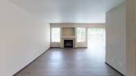 This two-story residence located in Tacoma, Washington offers a well-organized layout spread across two levels, connected by a staircase with a wood-railed banister. The entry-level hallway, finished with light wood-tone luxury vinyl plank flooring, leads toward the main living area, which features a fireplace visible from the corridor.

The kitchen is designed with white shaker-style cabinetry, light granite-look countertops, a peninsula with a breakfast bar overhang, stainless steel appliances including a range, refrigerator, and built-in range hood, along with a stainless steel double sink. The open sightlines between the kitchen and living area support an efficient, functional flow.

Two bathrooms mirror each other in finish, each featuring a tub-shower combination with stone-look tile surround, a white vanity with granite-look countertop, and light wood-tone flooring. The bedrooms are carpeted, providing comfort underfoot, and one features a bay window configuration that brings in generous natural light and views of surrounding greenery. Additional highlights include a baseboard heating unit and an attached garage with an automatic opener and electrical panel access.