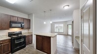 Located at 200 Citygreen Way in Chattanooga, Tennessee, this one-bedroom, one-bathroom residence offers a well-designed single-floor layout that maximizes its comfortable living footprint. The kitchen is a standout feature, showcasing rich dark-wood cabinetry, granite countertops, black appliances including an electric range and refrigerator, and a central island with pendant lighting above. The hardwood-style flooring throughout the kitchen and living areas adds warmth and visual continuity, while the open layout allows the kitchen to flow naturally toward the main living space, which is brightened by a large window. The spacious primary bedroom is finished with soft wall-to-wall carpeting and features a ceiling fan with integrated lighting, along with windows fitted with blinds that allow for excellent natural light and outdoor views. A dedicated closet provides practical storage within the bedroom. The bathroom is clean and functional, featuring a full tub-and-shower combination with brushed nickel fixtures. Neutral tones throughout the unit create a bright, cohesive aesthetic. The layout is efficient and thoughtfully arranged, making excellent use of the available space across every room.