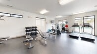 This 650-square-foot exercise room, located at 455 Racine Dr in Wilmington, NC, is a well-equipped fitness center designed to meet various workout needs. The space features a clean, modern aesthetic with white walls and a durable gray floor, creating a bright and inviting atmosphere. Fluorescent lighting fixtures are strategically placed throughout the ceiling to ensure proper illumination.

The gym is outfitted with a comprehensive range of exercise equipment, including cardiovascular machines such as treadmills, ellipticals, and stationary bikes. For strength training, there are weight machines, free weights with a multi-tier dumbbell rack, and adjustable benches. The layout allows for efficient use of space while maintaining ample room for movement between stations.

Large windows provide natural light and potentially offer views of the surrounding area. The room is equipped with climate control systems and includes amenities such as a wall-mounted TV, full-length mirror, and exercise balls for functional training. Safety features like a fire extinguisher and emergency exit are visible, ensuring a secure environment for users. The overall design prioritizes functionality and cleanliness, creating an ideal setting for diverse fitness routines.