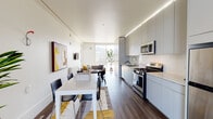 Located at 2201 Dwight Way in Berkeley, California, this single-floor unit offers a thoughtfully designed layout with a clean, modern aesthetic. The open-concept living, dining, and kitchen area runs the length of the unit, anchored by rich wood-tone flooring and bright white walls that maximize the sense of light and space. A large sliding glass door at the far end of the living area frames outdoor views and floods the interior with natural light, creating an airy, welcoming atmosphere. The kitchen is well-appointed with flat-front gray cabinetry extending floor to ceiling, stainless steel appliances including a gas range, microwave, and full-size refrigerator, and light-toned countertops. Subtle LED accent lighting runs along the upper cabinets, adding a contemporary touch. The dining area comfortably accommodates a full table and chairs, while the living space features a wall-mounted TV and access to the outdoor area. Multiple private bedrooms offer a quiet retreat, each finished with wood-look flooring and natural light from individual windows. The bathrooms are clean and functional, featuring a tub-shower combination, wood-look vinyl flooring, and a well-lit vanity. The unit's consistent neutral palette and modern finishes create a cohesive, functional living environment well-suited to Berkeley's vibrant residential community.