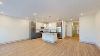 Located at 1130 Annondale Way in Fayetteville, NC, this well-appointed two-story home offers three bedrooms, three bathrooms, and a thoughtfully designed layout spread across two floors. The main level serves as the social hub of the home, anchored by an open-concept kitchen, dining, and living area. The kitchen is a standout, featuring a large center island with granite countertops and an undermount sink, two-tone cabinetry in white and slate gray, stainless steel appliances, and elegant pendant lighting — all complemented by light hardwood-style flooring and recessed lighting throughout. An attached garage with automatic opener provides convenient access, while a utility and laundry room add functional storage. The staircase is a design highlight, showcasing rich wood treads paired with a crisp white balustrade and dark wood handrail. Upstairs, the more generously proportioned floor houses all three bedrooms, including a well-sized primary suite. The primary bathroom features stone-topped white cabinetry with matte black hardware and a glass-enclosed shower. Secondary bedrooms offer plush carpet flooring, ceiling fans, and natural light from large windows with tree-lined views. Multiple closets and hallways provide ample storage throughout. The home presents a clean, modern aesthetic with neutral tones, quality finishes, and a cohesive design sensibility.