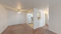 This single-floor, 2-bedroom, 1-bathroom unit offers a practical and efficiently arranged layout. The combined living room and kitchen area forms the heart of the space, where a ceiling fan overhead and baseboard heating provide year-round comfort. The living area features neutral-toned carpet and white walls, creating a clean, move-in-ready aesthetic. A front entry door opens directly into this open space, which connects seamlessly to the kitchen via a pass-through window opening. The kitchen is equipped with white cabinetry, a coil electric range with an over-the-range microwave, a full-size refrigerator, and ample counter space with a neutral laminate surface and tile flooring.

Both bedrooms are carpeted and finished in neutral tones, each supported by baseboard heating. The primary bedroom receives natural light through a large window fitted with vertical blinds. A dedicated closet features built-in shelving and double doors for organized storage. The second bedroom is comparably sized and similarly finished.

The bathroom is bright and clean, featuring tile flooring, a full-size soaking tub with a tiled shower surround, a toilet, and a vanity with counter space. A window with vertical blinds allows natural light into the room.