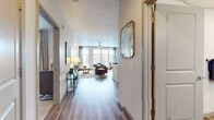 This thoughtfully designed single-floor residence offers a seamless blend of modern aesthetics and functional living. A welcoming entry hallway with wood-look plank flooring leads into the open-concept living and dining areas, where large windows flood the space with natural light and provide views of the surrounding neighborhood. The living room features neutral tones accented by contemporary décor, a ceiling fan, and generous room for entertaining.

The kitchen is well-appointed with stainless steel appliances including a refrigerator, range, microwave, and dishwasher, complemented by two-tone cabinetry, white quartz countertops, a tile backsplash, and pendant lighting above the kitchen island. The dining area sits adjacent, illuminated by natural light from floor-to-ceiling windows with stylish draping curtains.

The bedroom is a serene retreat finished with plush carpeting, large windows, and direct access to a spacious walk-in closet with built-in shelving and hanging storage. The bathroom offers a full tub-shower combination with tile surround, a dark-toned vanity with white countertop, and wood-look flooring that ties the space together cohesively.

Throughout the residence, clean lines, high ceilings, and a consistent modern palette create an inviting and polished atmosphere.