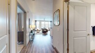 This thoughtfully designed single-floor residence offers a seamless blend of modern aesthetics and functional living. A welcoming entry hallway with wood-look plank flooring leads into the open-concept living and dining areas, where large windows flood the space with natural light and provide views of the surrounding neighborhood. The living room features neutral tones accented by contemporary décor, a ceiling fan, and generous room for entertaining.

The kitchen is well-appointed with stainless steel appliances including a refrigerator, range, microwave, and dishwasher, complemented by two-tone cabinetry, white quartz countertops, a tile backsplash, and pendant lighting above the kitchen island. The dining area sits adjacent, illuminated by natural light from floor-to-ceiling windows with stylish draping curtains.

The bedroom is a serene retreat finished with plush carpeting, large windows, and direct access to a spacious walk-in closet with built-in shelving and hanging storage. The bathroom offers a full tub-shower combination with tile surround, a dark-toned vanity with white countertop, and wood-look flooring that ties the space together cohesively.

Throughout the residence, clean lines, high ceilings, and a consistent modern palette create an inviting and polished atmosphere.