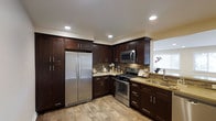The kitchen serves as a central highlight of this single-story space, showcasing a thoughtfully designed layout that balances functionality and aesthetics. Rich, dark espresso-toned shaker-style cabinetry lines the walls from floor to ceiling, providing generous storage while creating a bold visual contrast against the light, neutral walls and warm-toned luxury vinyl plank flooring.

Stainless steel appliances, including a French door refrigerator, gas range with microwave above, and an undermount sink, lend a sleek, contemporary feel. The textured tile backsplash adds dimension and visual interest, complementing the warm-toned countertops that run throughout the workspace. Recessed lighting overhead ensures the kitchen is well-lit, while a window above the sink invites natural light, brightening the space during the day.

The L-shaped layout maximizes counter space and promotes an efficient workflow, making it well-suited for both everyday cooking and entertaining. Overall, the kitchen exudes a modern yet warm ambiance, combining durable, practical finishes with refined design details.