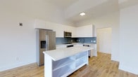 Located at 309 South 4th Street in the heart of Columbus, Ohio, this modern single-floor residence delivers a clean, contemporary aesthetic throughout. The kitchen serves as the centerpiece of the space, showcasing a bright, open layout with high-gloss white cabinetry that extends toward the elevated ceilings, maximizing storage while contributing to an airy, expansive feel. A large central island with a crisp white countertop provides ample workspace and open shelving below for additional storage and display. The kitchen is equipped with stainless steel appliances, including a French door refrigerator with ice and water dispenser, a built-in microwave, and a dishwasher. A stylish blue-gray subway tile backsplash adds a subtle pop of color and texture, complementing the neutral palette. Light-toned hardwood flooring runs throughout, enhancing the sense of warmth and continuity across the space. The tall ceilings lend a sense of volume and openness, making the interior feel bright and welcoming. The overall design blends functionality with a refined minimalist style, ideal for those seeking a well-appointed, move-in ready space in Columbus's vibrant South Fourth Street corridor.