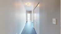 This well-appointed high-rise residence offers 2 bedrooms and 2 bathrooms across a single floor of generously proportioned living space. Floor-to-ceiling windows throughout flood the interior with natural light and frame dramatic panoramic views of the city skyline and lake beyond. The open living area features dark hardwood flooring and direct access to a large tiled balcony enclosed by glass railings, offering unobstructed views in multiple directions. The modern kitchen is equipped with a central island, sleek gray wood cabinetry, dark stone countertops, black appliances including a gas range and dishwasher, and pendant lighting — all complemented by large windows that maximize natural light. The spacious primary bedroom features plush carpeting, a built-in closet, and expansive windows showcasing lake and city views. The second bedroom is equally well-lit with floor-to-ceiling windows overlooking the skyline. The primary bathroom is finished with rich dark marble tile on the floors and walls, and includes both a soaking tub and a glass-enclosed shower. The second bathroom offers a clean, classic design with cream-toned tile surrounding the tub and shower. A hallway with blue-toned flooring and built-in storage connects the living spaces to a welcoming entrance, completing this thoughtfully designed residence.