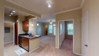 This single-story residence at The Lakes At Cypresswood in Houston, Texas offers a well-designed, open-concept layout finished with consistent neutral tones and warm accents throughout. Crown molding lines the living and common areas, complementing the plush carpeting that extends across the main living spaces and bedrooms, while tile flooring is found in the kitchen and bathroom areas.

The kitchen is equipped with rich wood cabinetry, dark granite-style countertops, black appliances including a refrigerator, range, and built-in microwave, and a peninsula with a double-basin sink. Pendant lighting and track lighting illuminate the workspace, which opens directly to the living area through a pass-through counter arrangement.

The living room is spacious and bright, featuring a ceiling fan, crown molding, and an exterior door with sidelight windows that invite natural light. An arched doorway leads to a built-in nook, adding a decorative architectural detail. The bedroom is generously proportioned, featuring a ceiling fan, a window with outdoor views, and access to a walk-in closet with built-in shelving.

The bathroom features tile flooring, a full tub-shower combination with tile surround, wood vanity cabinetry, and granite-style countertops, maintaining the cohesive material palette found throughout the residence.