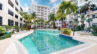 Located at 805 North Olive Avenue in West Palm Beach, Florida, this compact single-room space is part of a vibrant, resort-style residential community in the heart of downtown West Palm Beach. While the interior space itself is modest in footprint, it is situated within a striking multi-story building complex that boasts impressive outdoor amenities. The centerpiece of the community is a large, sparkling resort-style swimming pool surrounded by lush tropical landscaping, including tall royal palms and colorful tropical plantings that evoke a quintessential South Florida atmosphere. The pool deck is lined with lounge chairs, offering residents a relaxing outdoor retreat under the warm Florida sun. The surrounding architecture features a clean, modern aesthetic with white facades, multiple stories of residential units, and private balconies overlooking the pool courtyard. The open-air setting allows for abundant natural light and a seamless connection between the interior and the vibrant outdoor environment. Positioned in West Palm Beach's urban core, the property benefits from convenient access to the city's cultural, dining, and entertainment offerings, making it a desirable location for those seeking a dynamic South Florida lifestyle.