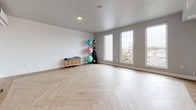 Located at 3240 Hollis St in Oakland, CA, this single-floor fitness and wellness studio offers a clean, contemporary environment well-suited for yoga, group exercise, or personal training sessions. The space is defined by its striking herringbone-patterned wood flooring, which adds visual warmth and texture to an otherwise minimalist interior finished in neutral gray tones with crisp white baseboards.

The open layout provides generous, unobstructed floor space, making it highly adaptable for a variety of fitness formats. A wall-mounted yoga mat storage rack keeps equipment organized and accessible, while a freestanding rack accommodates multiple exercise balls in varying sizes. A built-in mini-split air conditioning unit ensures year-round climate control and comfort for active use.

A bank of tall, vertically oriented windows along one wall draws in abundant natural light while framing elevated views of the surrounding Oakland neighborhood, creating an airy, uplifting atmosphere. A glass-paneled entry door connects the studio to adjacent areas and contributes to a sense of openness. The overall design is functional, modern, and well-equipped to support a dedicated wellness practice.